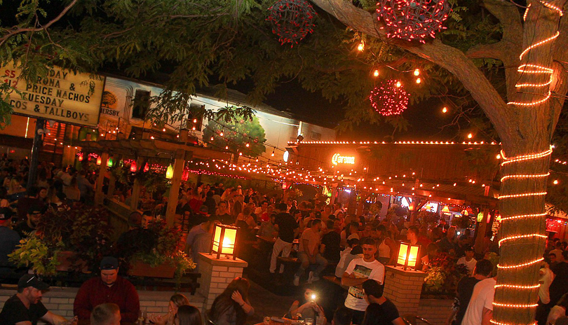 Large groups of people standing and sitting at an outdoor patio in the evening at Barney's and The Ceeps, located in London, Ontario, Canada