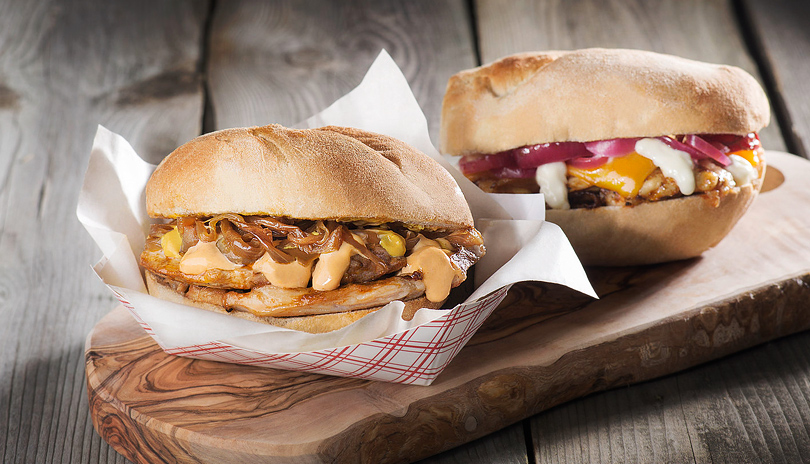 Two sandwiches on display from Bifana Boys food truck on a wooden plank