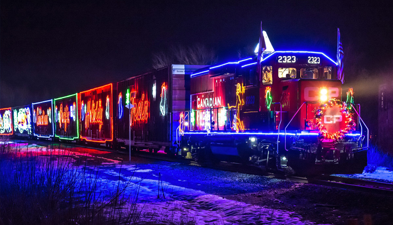 A train driving on railroad tracks at night decorated with holiday lights