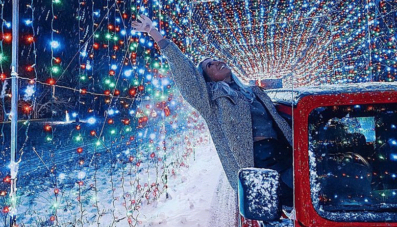 Woman hanging out of truck window admiring stringed Christmas lights.