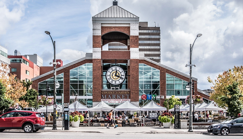 Front entrance view of Covent Garden Market with various outdoor vendors in tents selling fresh produce, located in London, Ontario