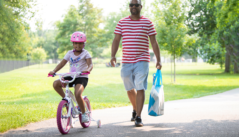 A father and his daughter biking down a paved path in Gibbons Park located in London, Ontario