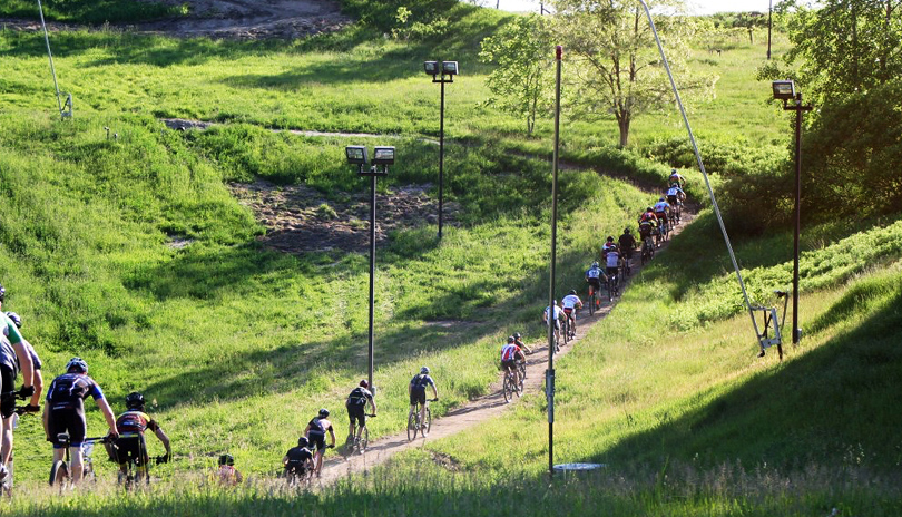 A large pack of mountain bike riders racing on a dirt path surrounded by greenery and forest in Boler Mountain located in London, Ontario