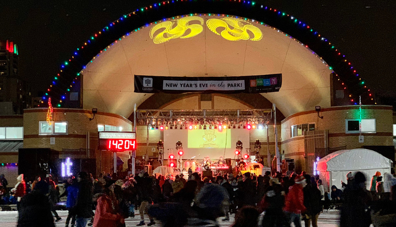 A live band playing at the outdoor bandshell in Victoria Park with people skating on the rink in front of it celebrating a new year's eve event in London, Ontario