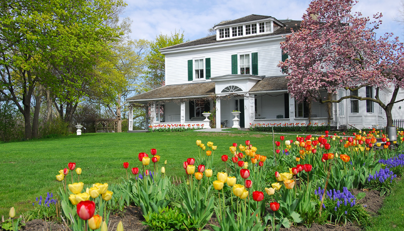 Exterior view of the front entrance of the Eldon House surrounded by colourful tulips and large trees in London, Ontario