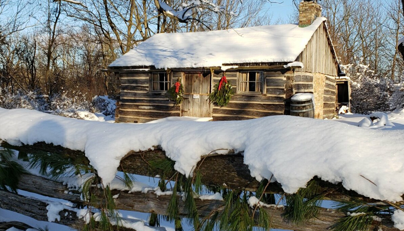 A snow covered historic cabin at Fanshawe Pioneer Village's Holiday Market in London, Ontario, Canada