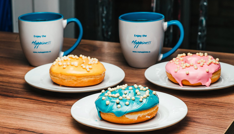 A table top with three colourful donuts on individual plates and two cups of coffee from Happiness a cafe in London, Ontario