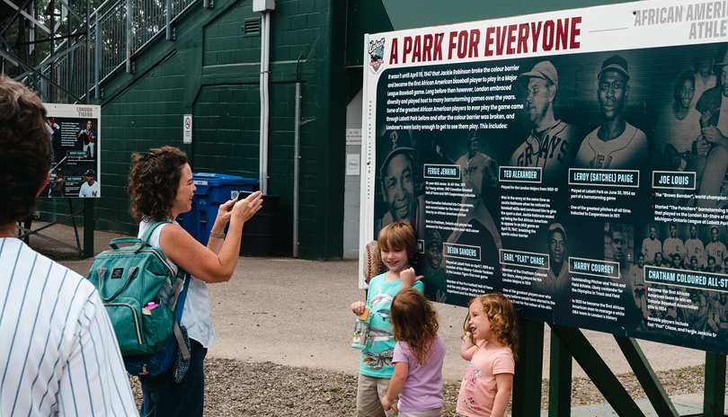 A mother taking a photo of her children in front of a a historic mural on display at Labatt Park, The World's Oldest Operating Baseball Grounds, located in London, Ontario, Canada