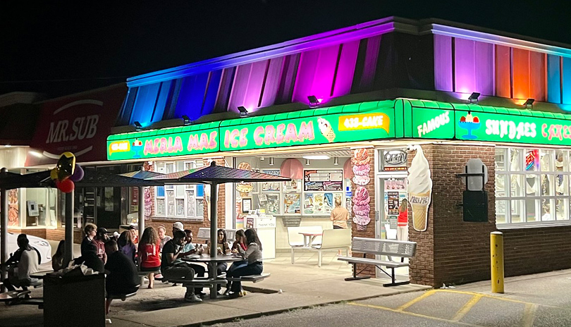 People siting at tables outdoors at night enjoying ice cream outside of Merla Mae Ice Cream's storefront