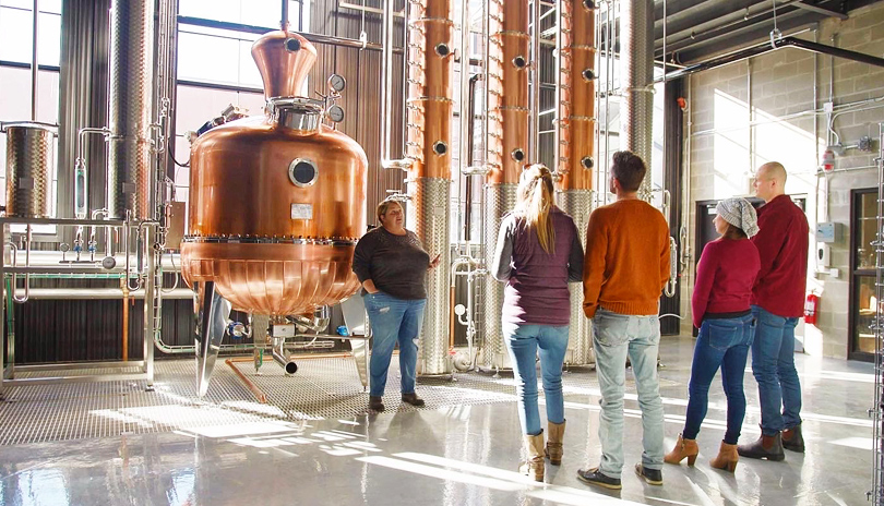 Four people taking a guided tour of Paradigm Spirits Co. production distillery room located in London, Ontario