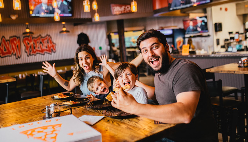 A happy family with children sitting at a table and enjoying pizza in Pizza Projekt located in London, Ontario