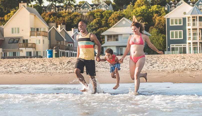 A husband and wife holding their child hands running into the water at Port Stanley's beach