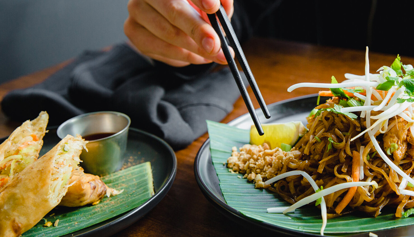 A hand with chopsticks about to eat from a plate of Thai food from Thaifoon Restaurant located in London, Ontario