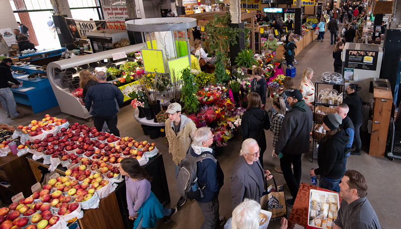 A crowd of people walking through The Market at Western Fair District with various vendors selling fresh produce, located in London, Ontario