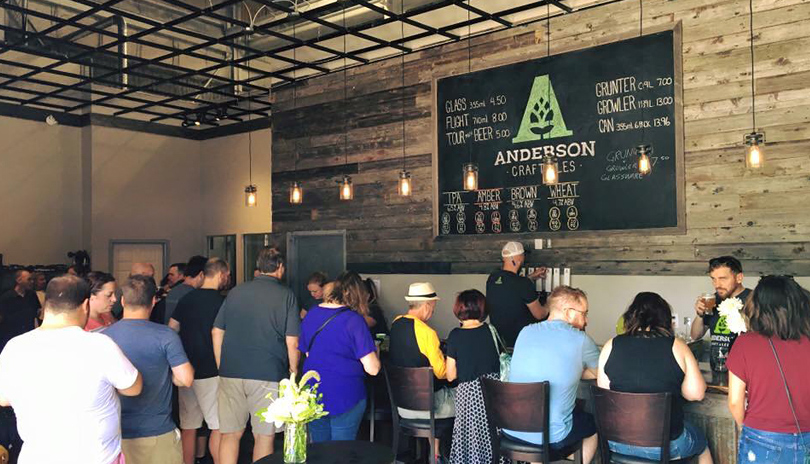 A large group of people seated at a bar and standing in Anderson Craft Ales main showroom located in London, Ontario