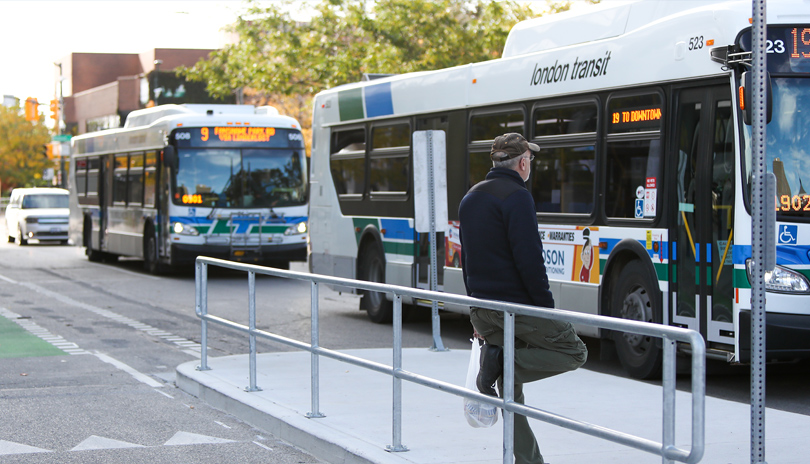 A man waiting at a bus stop with two busses approaching his location in London, Ontario
