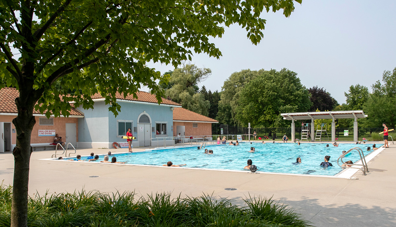 A large group of people swimming at the outdoor pool of Gibbons Park on a warm summer day located in London, Ontario