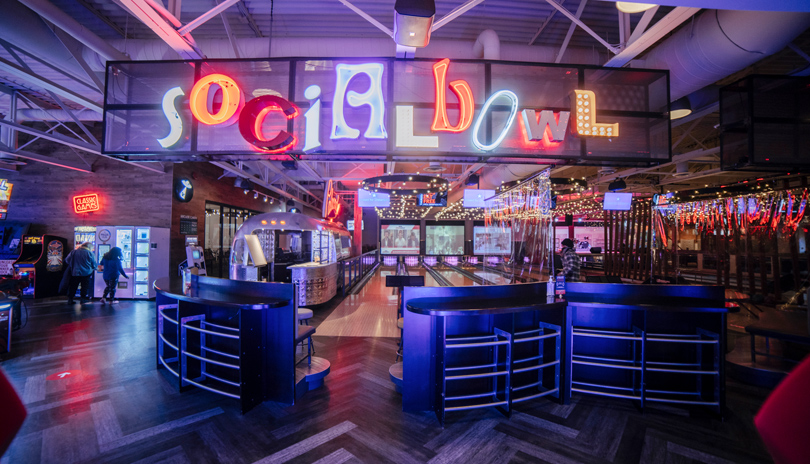 A colourful neon sign that reads Social Bowl with bowling lanes in the background and arcade located at Palasad Social Bowl in London, Ontario