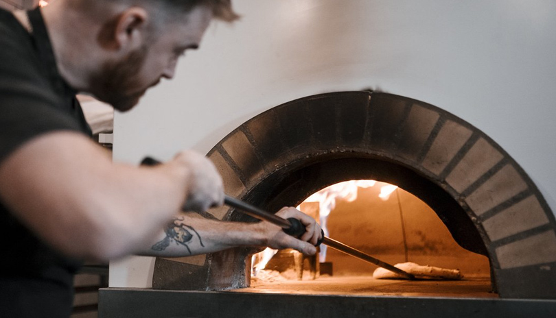 A chef pulling out a pizza from a wood burning oven in Pizzeria Madre located in London, Ontario