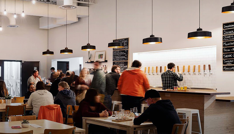 Groups of people seated at tables and standing at a bar in Storm Stayed Brewing Company's main showroom located in London, Ontario