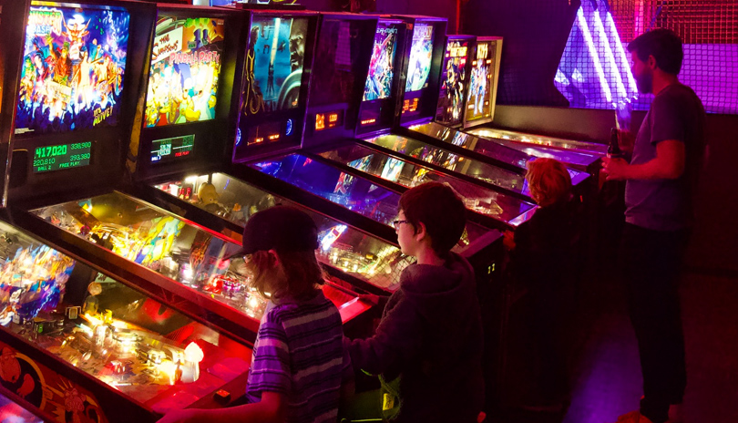 A father and his 3 children playing various Pinball machines in Tilt Arcade Bar located in London, Ontario.