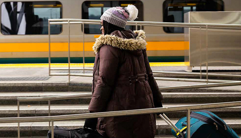 A woman dressed for Winter and pulling luggage about to board a VIA Rail train