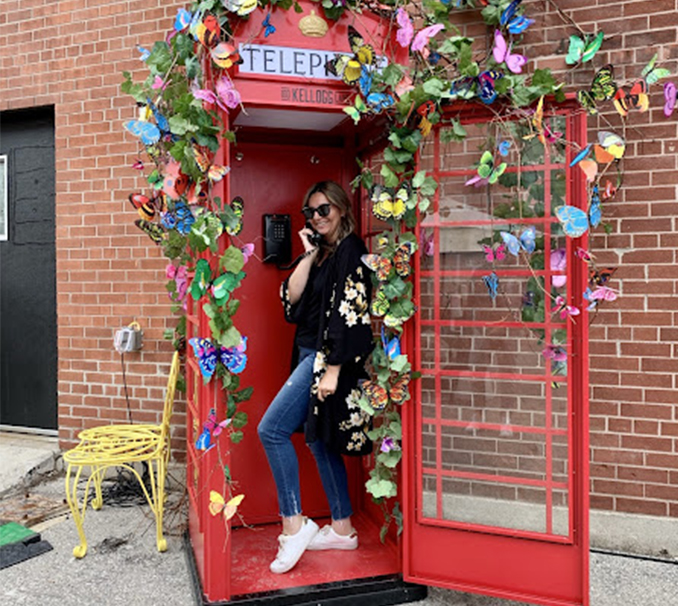 woman standing in vintage red telephone booth decorated in butterflies and flowers 