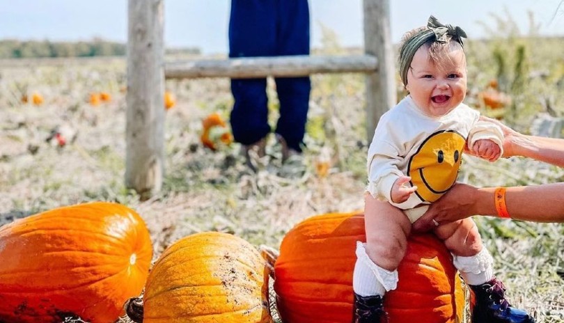 Infant child being held beside group of three pumpkins at clovermead adventure farm