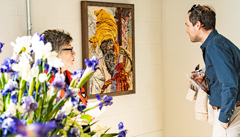 Man closely inspecting an artwork at 100 Kellogg Lane during the evetn Art Comp