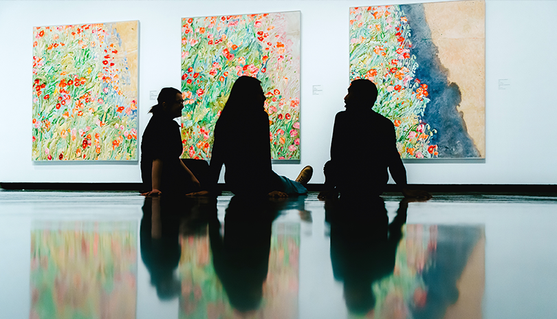 Three people viewing artwork of flowers at Museum London in London, Ontario