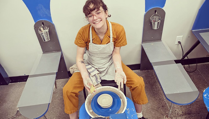 Women sitting in front of a rotating stand crafting pottery