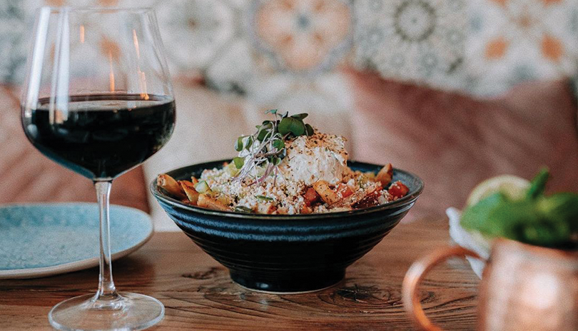 A bowl of greek food with a glass of red wine displayed on a table at Dimis Greek House