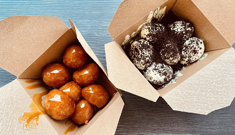 Two small boxes of doughbits, a doughy small pastry. One is drizzled in caramel while the other is covered in cookies and cream icing