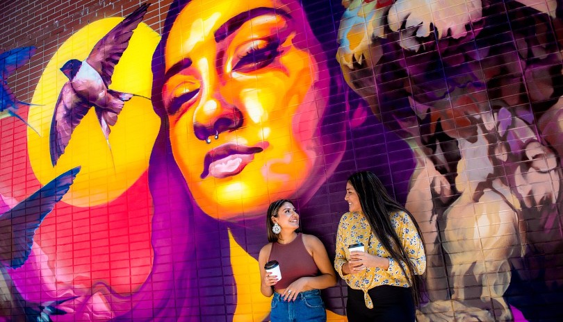 Two women sharing a smile at Market Lane by Covent Garden Market with a large outdoor mural behind them