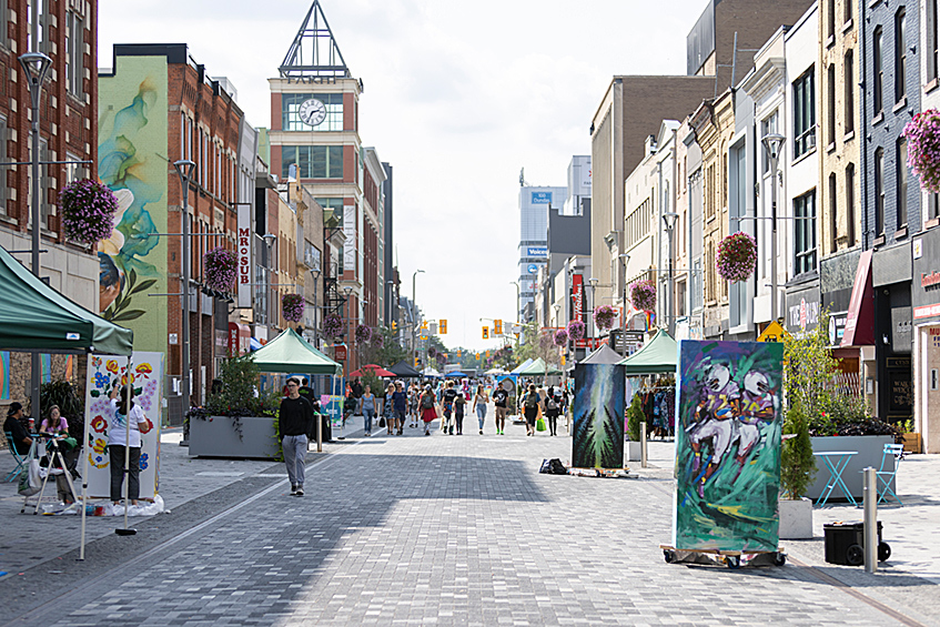 Various people walking down a closed off street with outdoor vendors and displays on Dundas Place located in downtown London, Ontario.