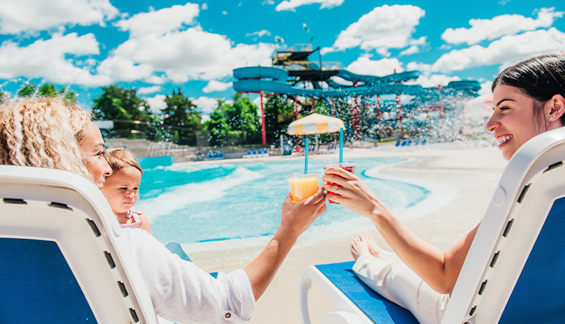 Two moms enjoying a drink by the pool at east pakr while the water slide is in the distance