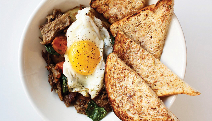 a fried egg over a breakfast hash with four half pieces of toast all displayed in a white bowl