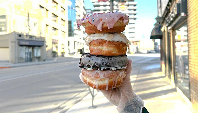 A stack of four icing glazed donuts outside of Commonwealth Coffee Co in London, Ontario