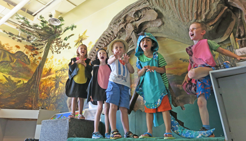 Five young kids dressed up as dinosaurs and playing in a dinosaur themed room in the London Children’s Museum located in London, Ontario