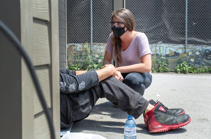A woman speaking to a homeless male sitting on a sidewalk in London, Ontario