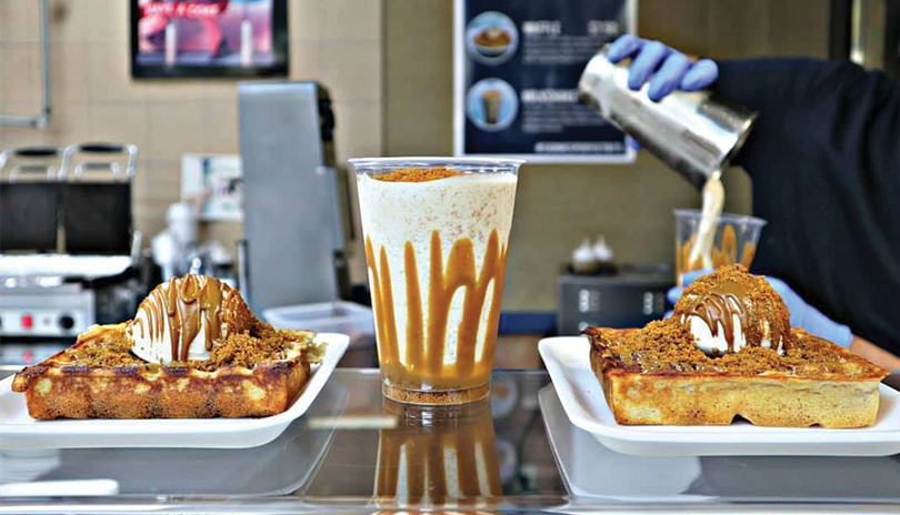 two waffles covered in ice cream, belgian cookie butter and biscuit toppings pictured with a milkshake