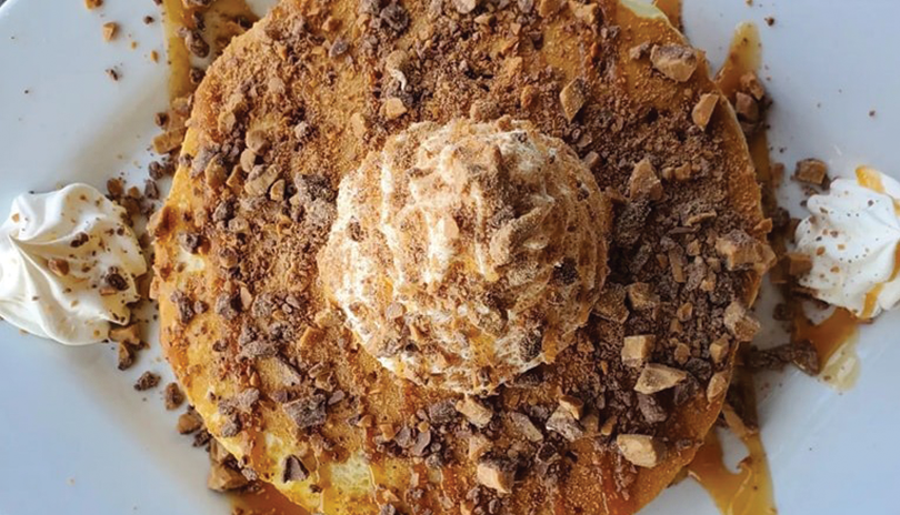 pancakes on a white plate covered with caramel sauce, skor bites and whipped cream