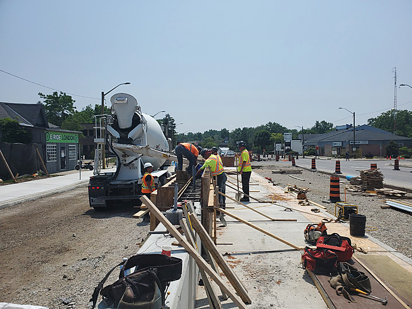 A group of construction workers pouring concrete and setting a sidewalk in London, Ontario