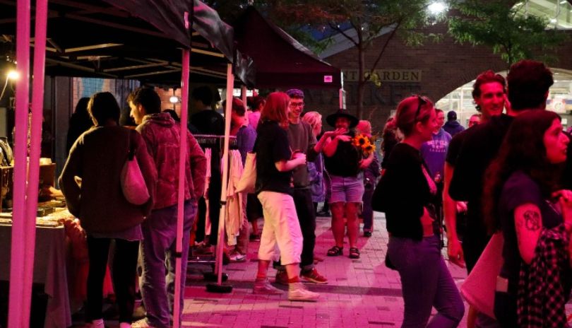 Evening market scene with tents vendors shoppers and bright pink purple lighting creating lively atmosphere