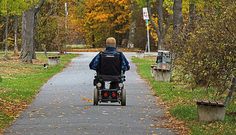 Man in wheelchair riding along a pathway in a park.