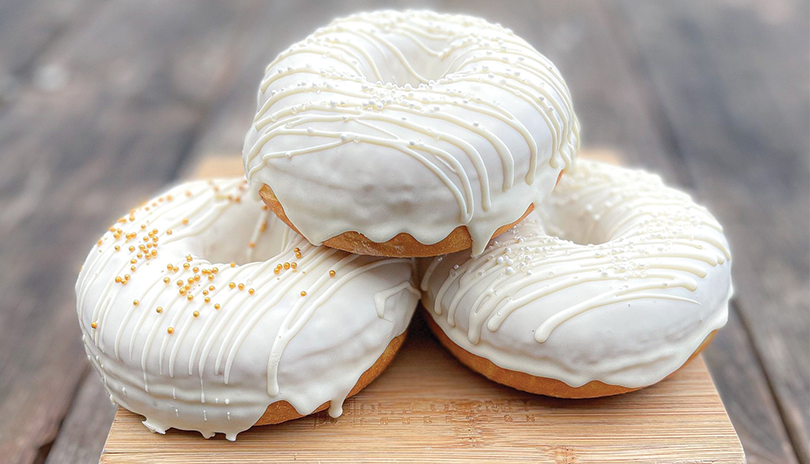 three donuts with white icing displayed on a wooden board