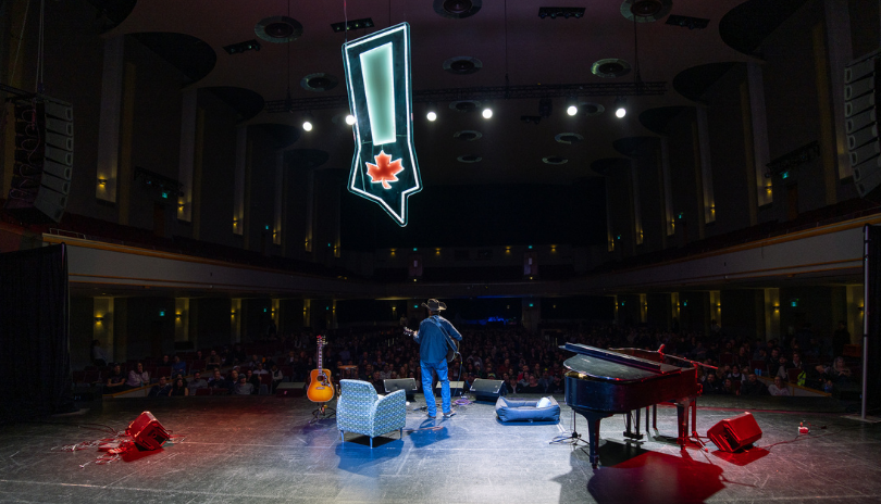 A man stands onstage in front of a large venue of people for a comedy show in London, Ontario.