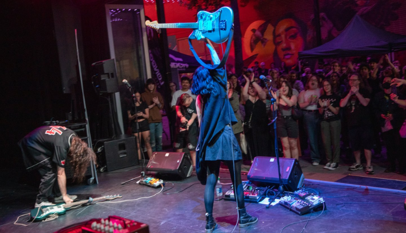 An artist holds a guitar in the air in front of a cheering crowd.
