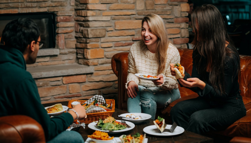 A group of friends eat tacos and other food around a low table at The Club House in London, Ontario.