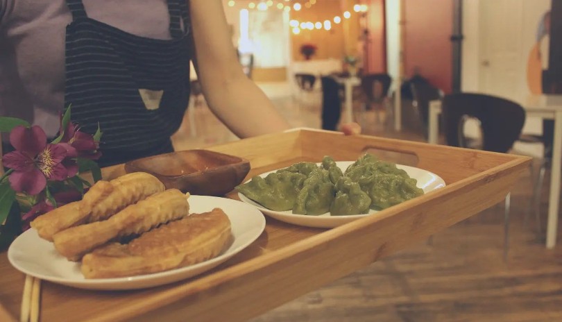 Woman bringing out tray of assorted dumplings